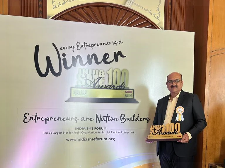 Dattatreya Lakshmi Narasimha holding the India SME 100 Awards trophy in front of a backdrop reading every Entrepreneur is a Winner, India SME 100 Awards, Entrepreneurs are Nation Builders, India SME Forum.