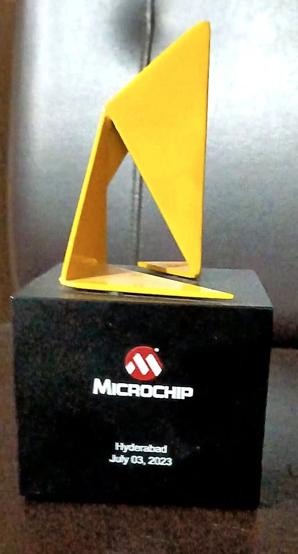 A yellow folded-sail sculpture on a black stone block lettered with the Microchip logo above the words Hyderabad, July 03, 2023.