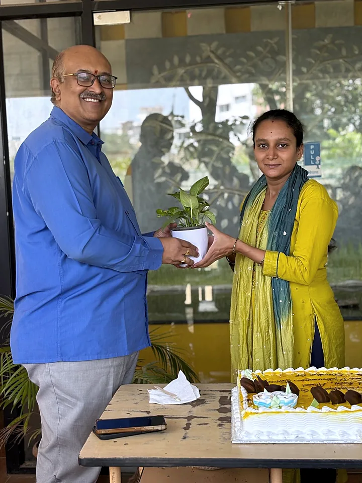 Two colleagues holding a potted plant together at the office entrance.