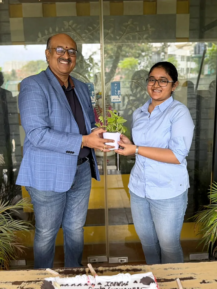 A colleague holding a potted plant with a senior colleague at the office door.