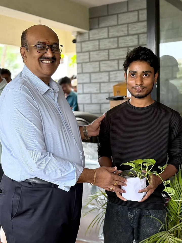 Two colleagues holding a potted plant on the office porch.