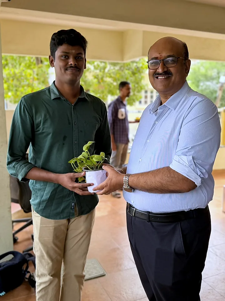 Two colleagues standing together with a potted plant outside the office.