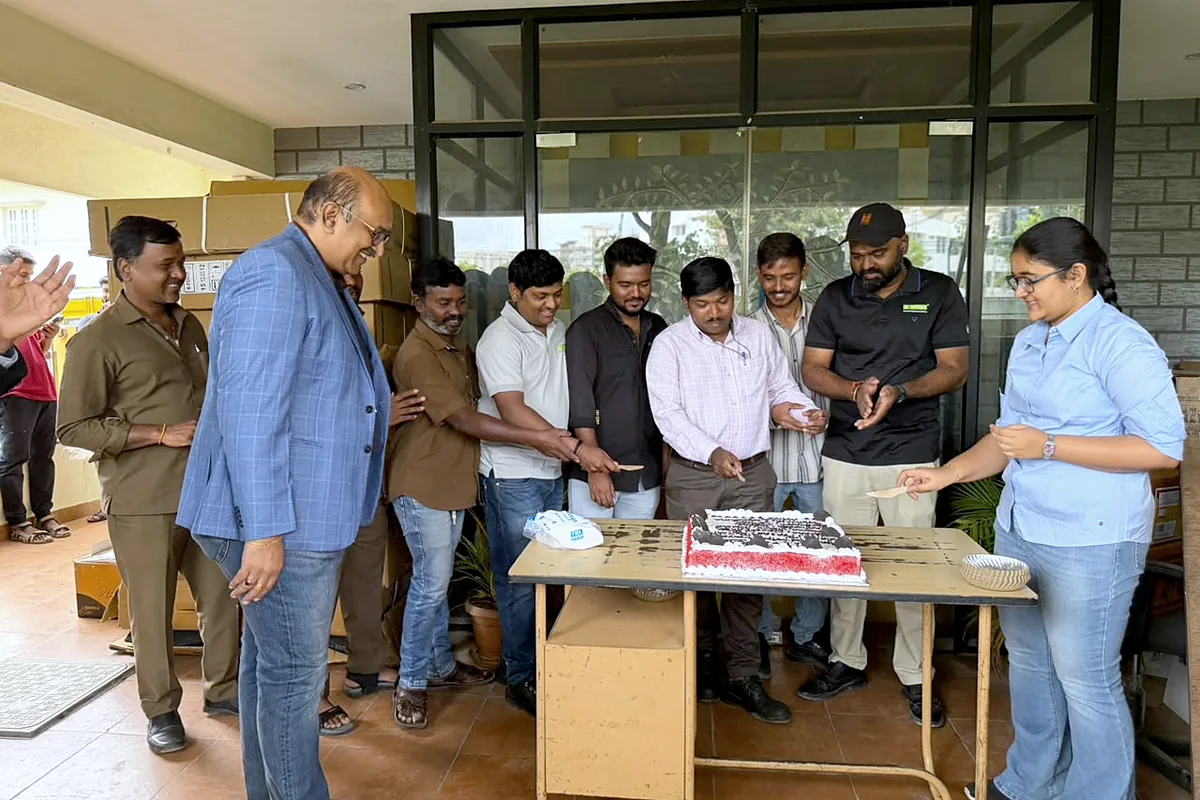 Colleagues gathered around the table on the porch, hands together on the knife, cutting a birthday cake.