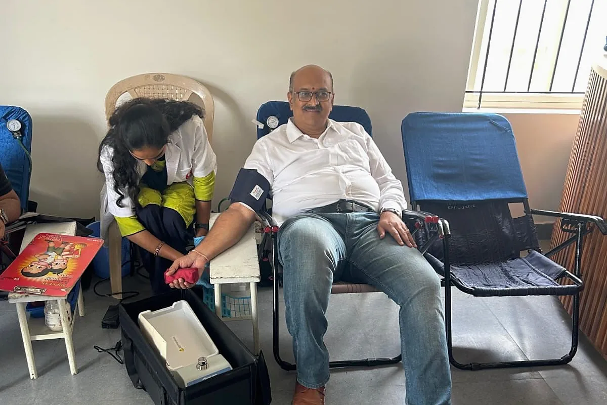 A donor seated with a pressure cuff on his arm while an attendant sets up the collection kit.