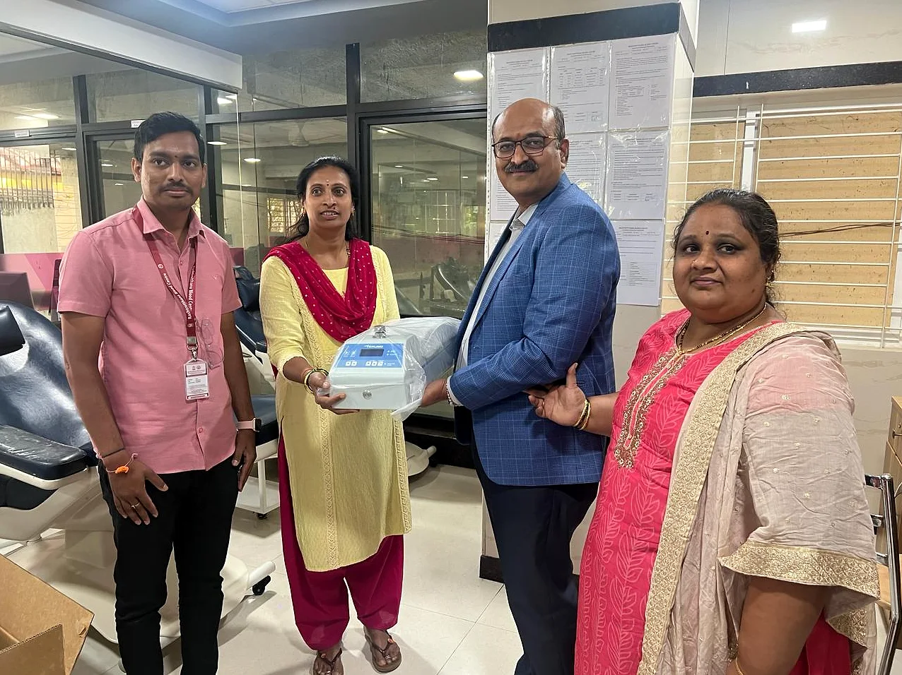 A boxed medical device handed over to clinic staff, the four of them holding it between them.