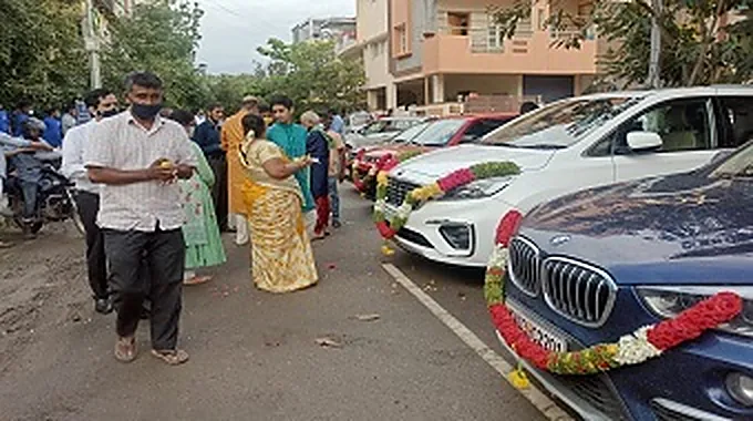 Garlanded cars lined up in the street for a company puja, with the team gathered alongside.