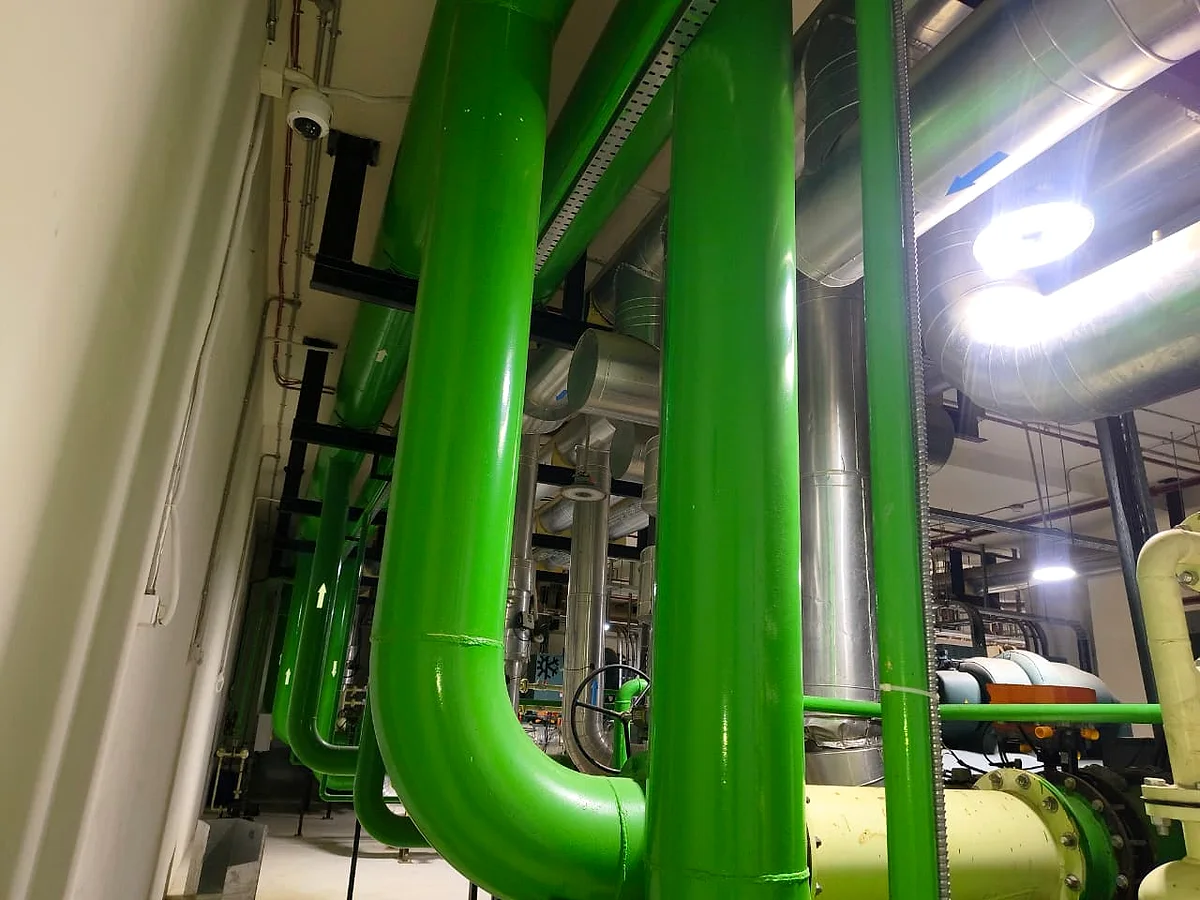 Green chilled-water risers sweeping up through the plant room ceiling beside lagged flow and return lines.